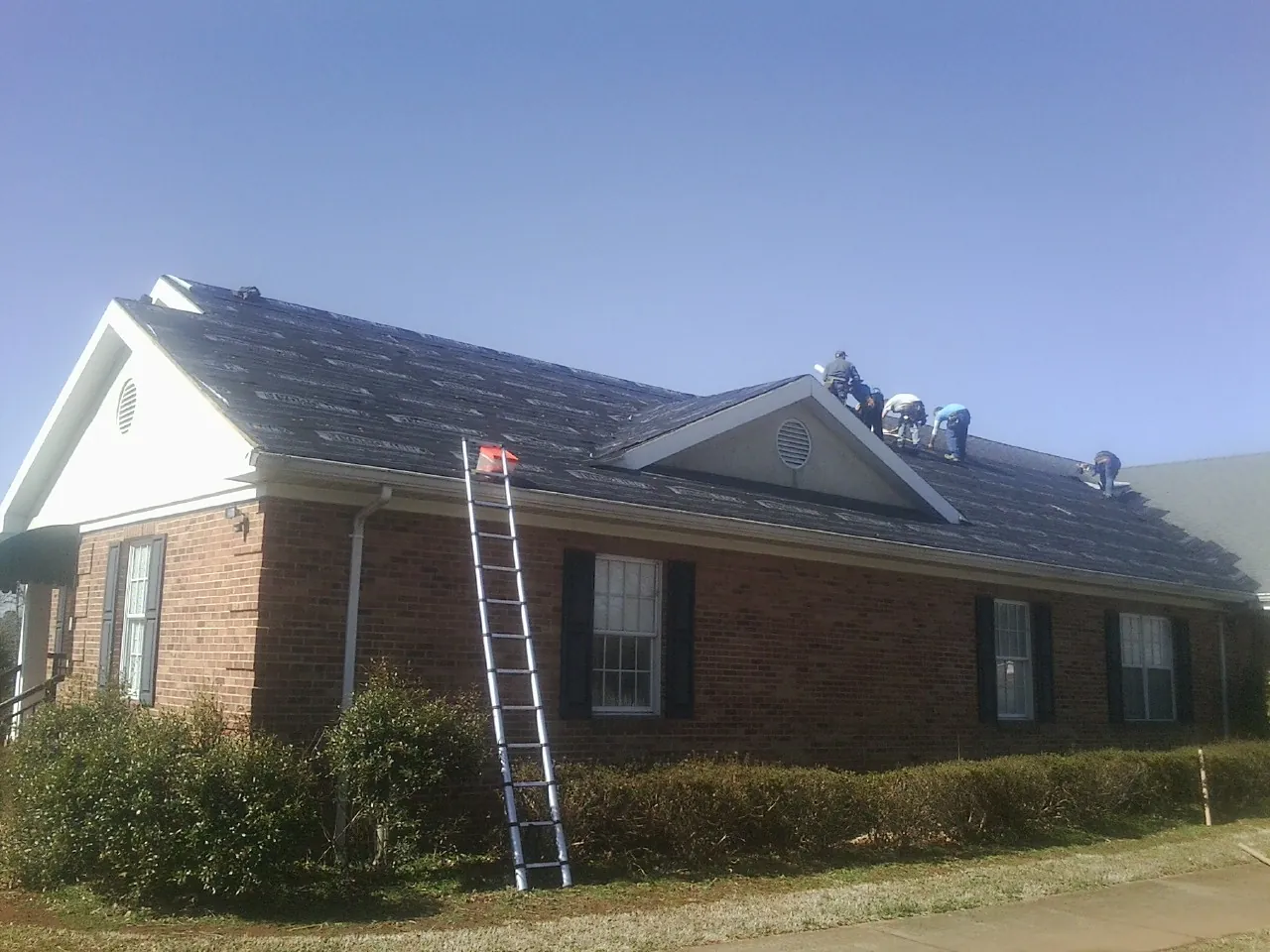 Crew tearing shingles off a brick ranch roof with a ladder set — Metal Roof Repair work by our crew in Brodheadsville