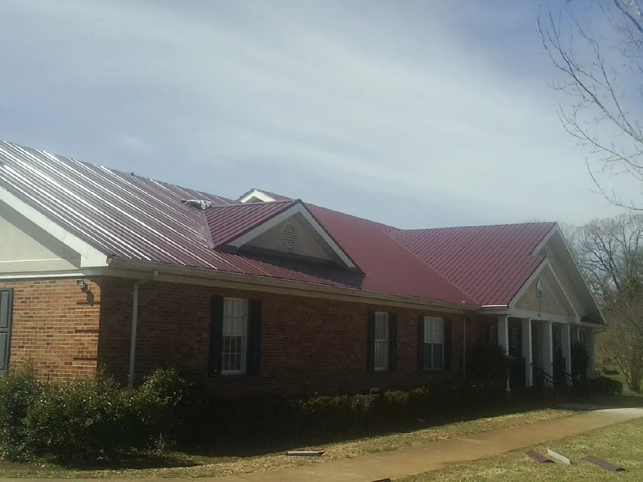 Red metal roof with gabled entries on a long brick building, from a Hail Damage Roof Repair job in Brodheadsville