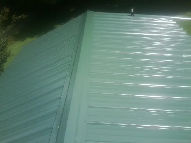 New green metal panels meeting at the ridge of a roof — Flat Roof Repair work by our crew in Brodheadsville