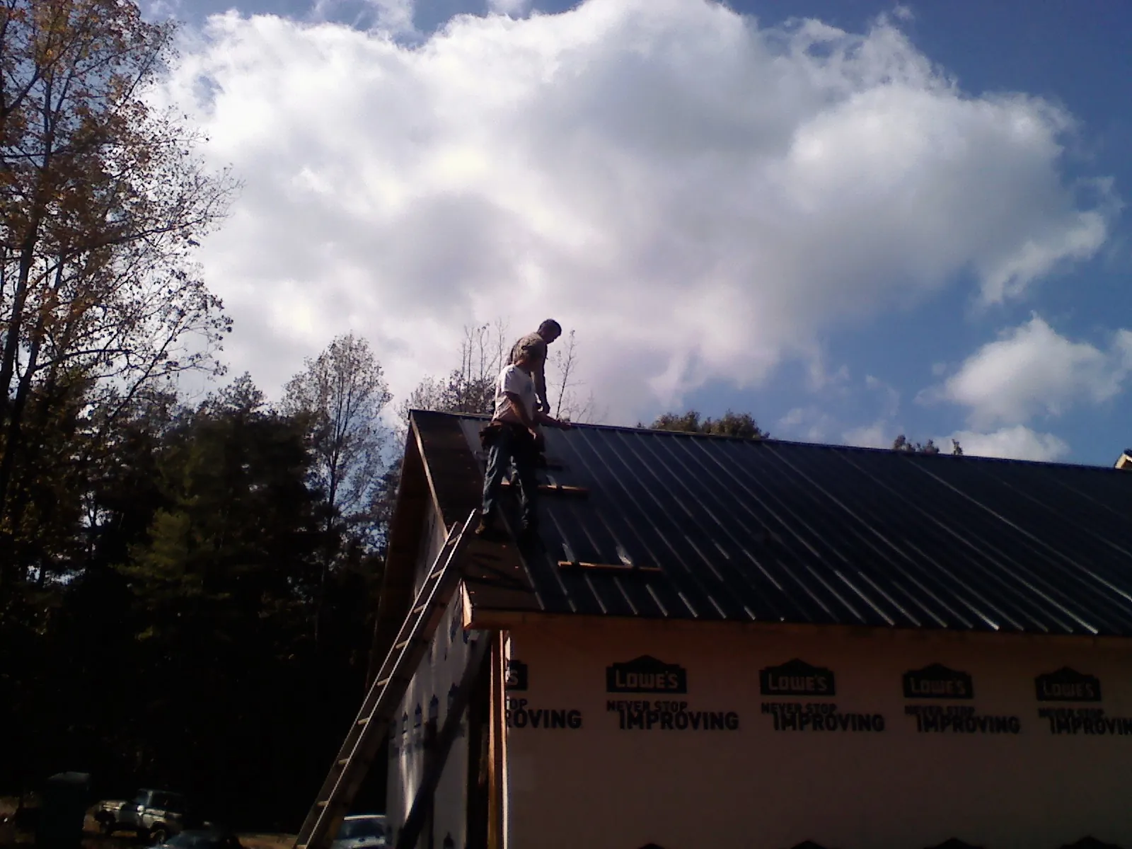 Roofer fastening dark metal panels high against a cloudy sky, from a Roof Inspection job in Brodheadsville