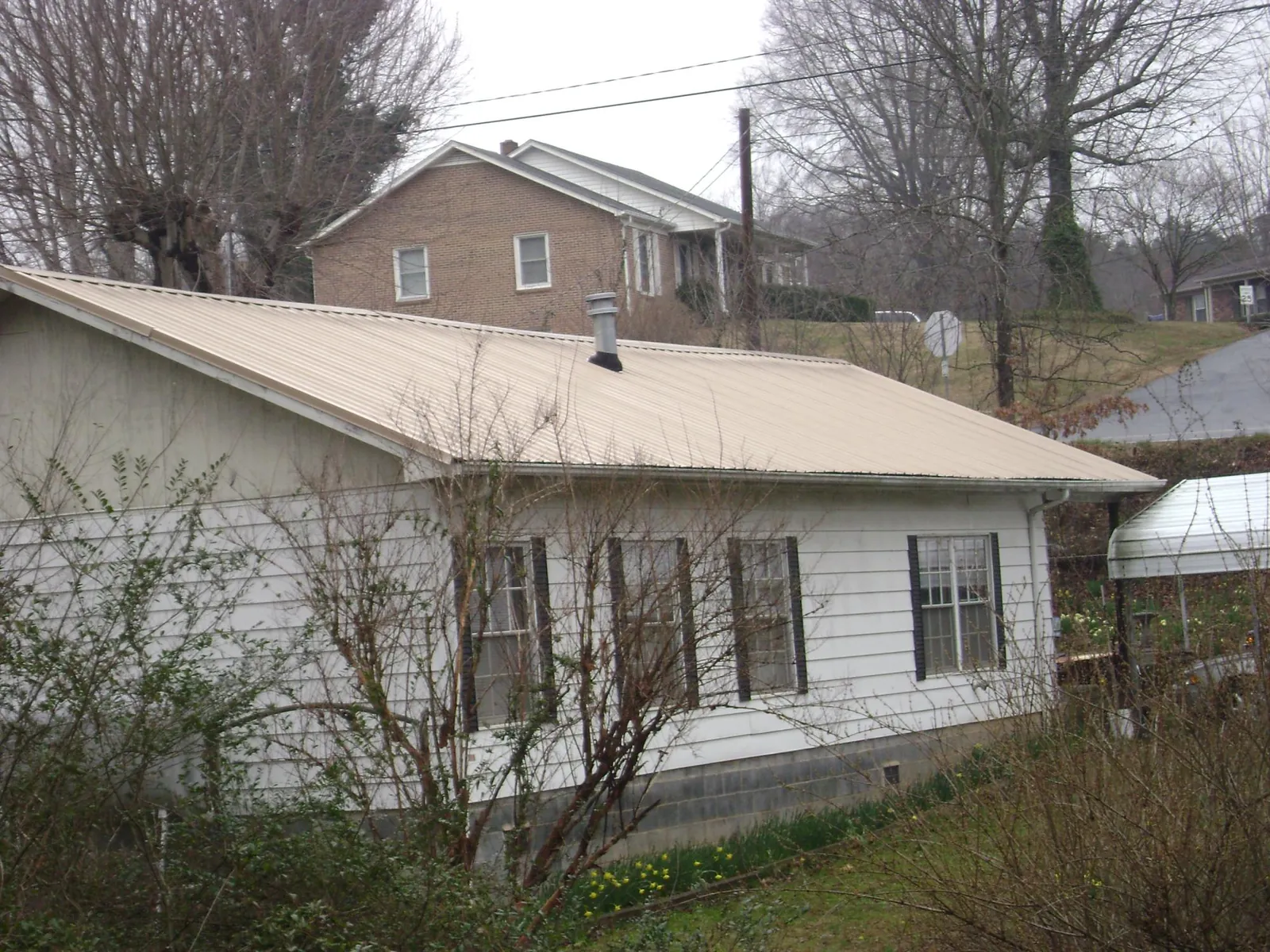Tan metal roof on a white sided house set into a hillside — Commercial Roofing by Roofing Brothers in Brodheadsville